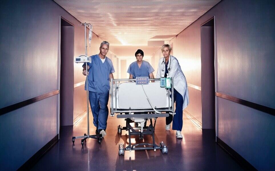 Doctor and 2 nurses with a Patient in a bed down the Hospital hallway 